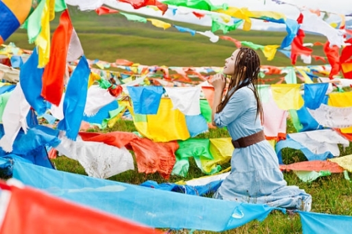 The tibetan girl praying before the prayer flags
