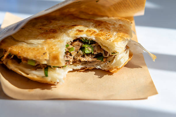 A close up of a Roujiamo or Chinese burger from Shannxi Province, China.
The bun is a multi layered, crispy flat bread, with the classic filling of spicy slow braised pork chopped with fresh herbs.
