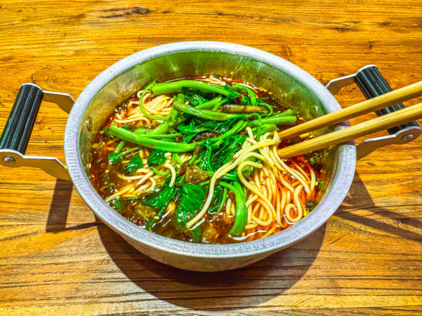 A steaming bowl of Chongqing Xiao Mian, featuring al dente noodles in a rich, spicy broth topped with fresh greens. This classic dish from Chongqing, China, is known for its bold flavors and comforting heat, offering a taste of authentic Chinese street food culture.
